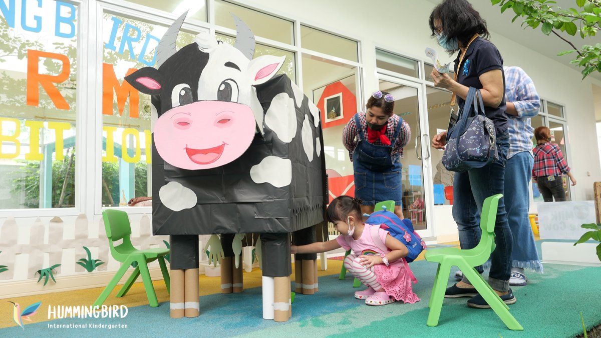 A group of people are standing around a cow made out of cardboard.
