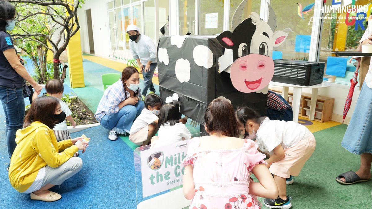 A group of children are playing with a cow made out of cardboard.