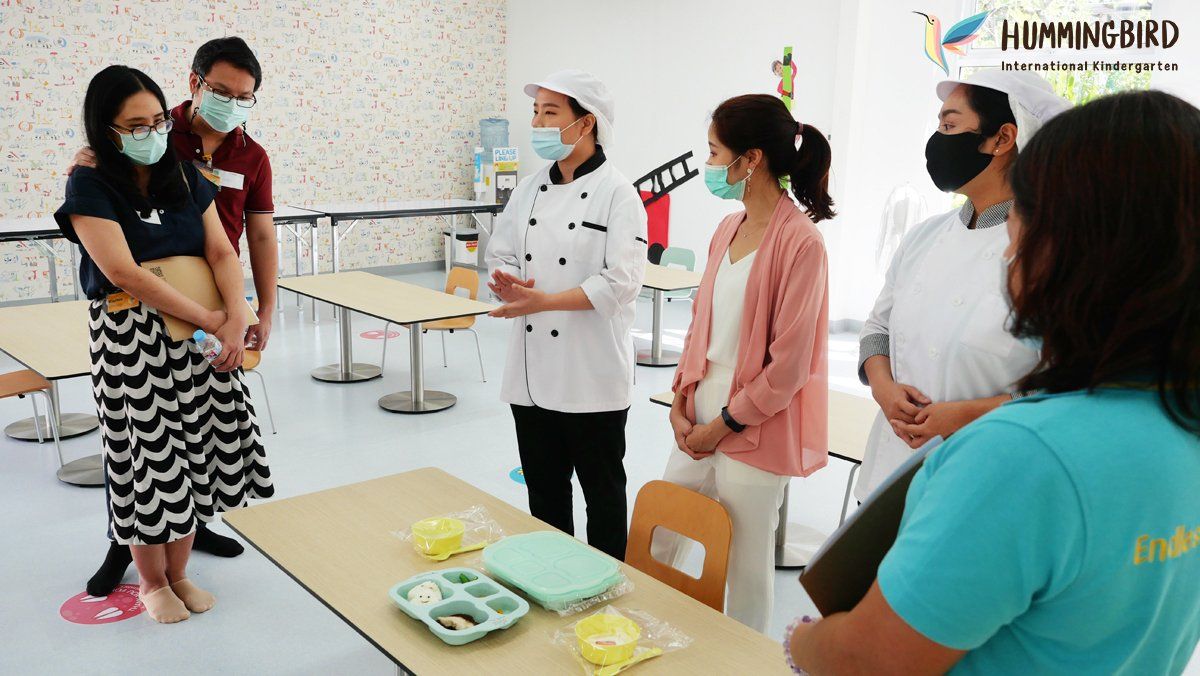 A group of people wearing face masks are standing around a table.