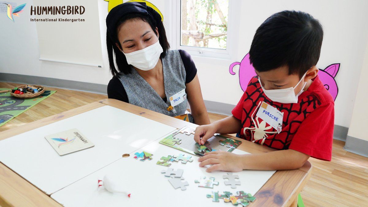 A woman and a boy wearing masks are sitting at a table playing with puzzles.