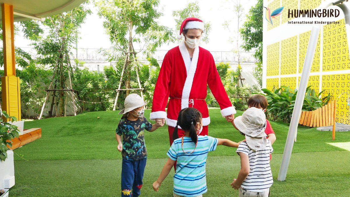 A man dressed as santa claus is holding hands with three children.