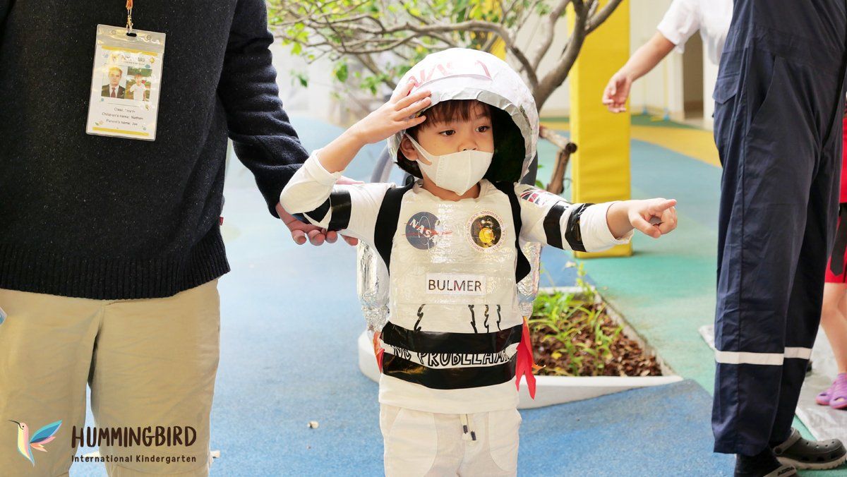 A little boy in an astronaut costume is saluting while holding a man 's hand.