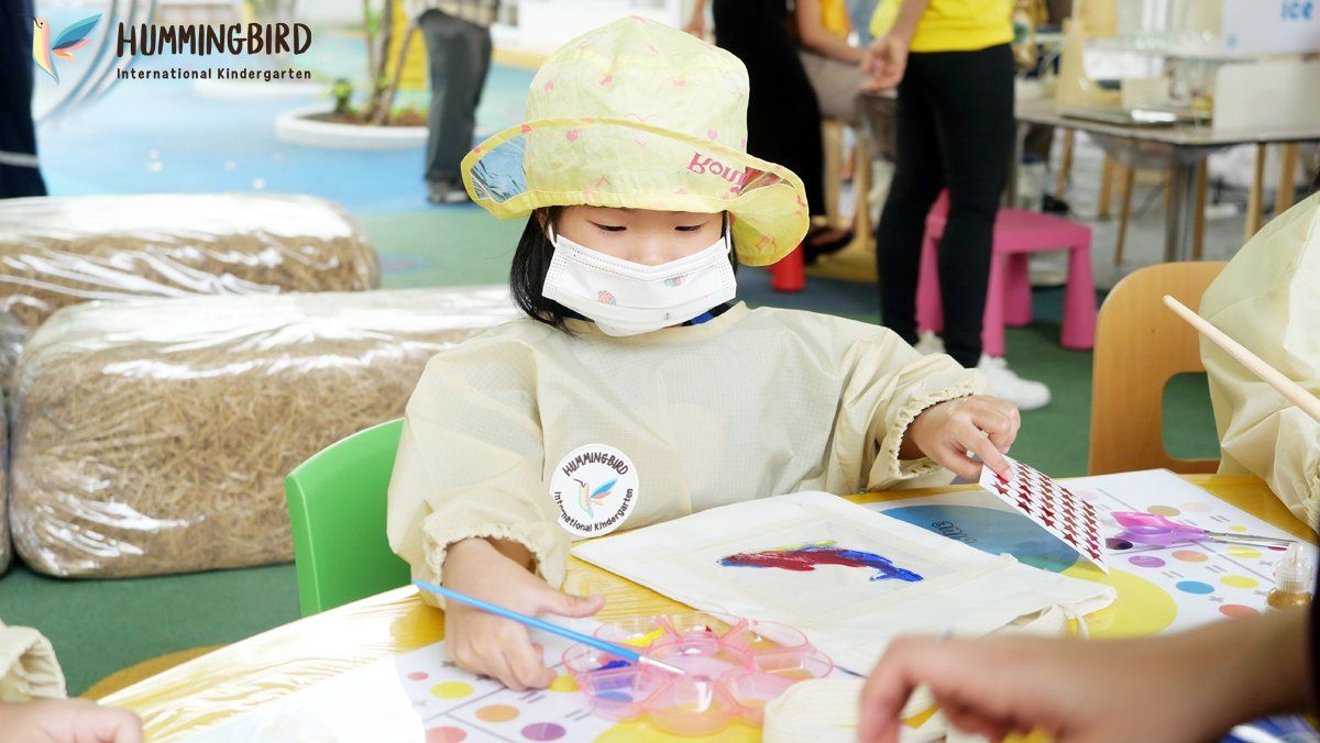 A little girl wearing a mask is sitting at a table painting.