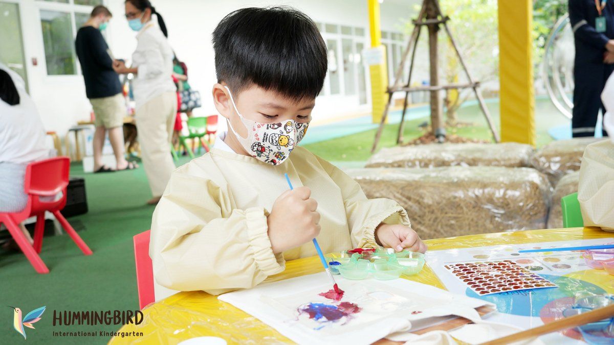 A young boy wearing a mask is painting at a table.