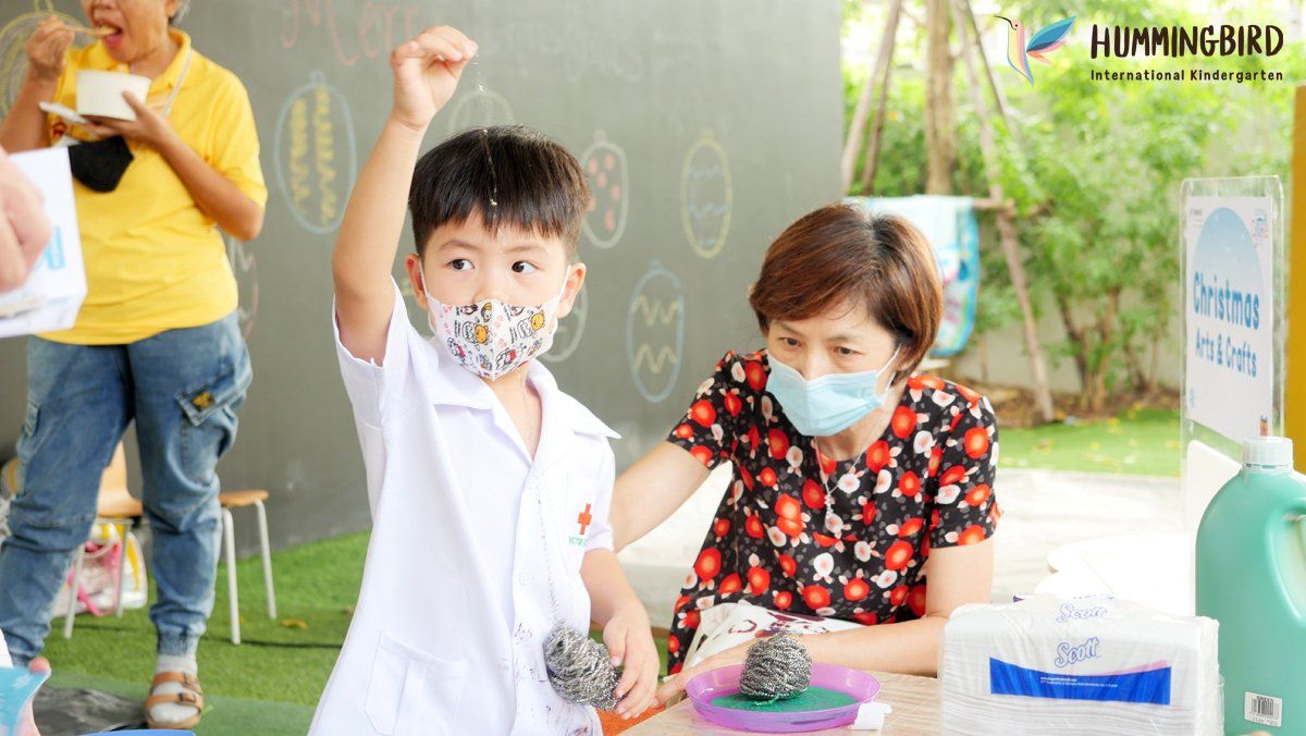 A little boy wearing a mask is sitting at a table with a woman.