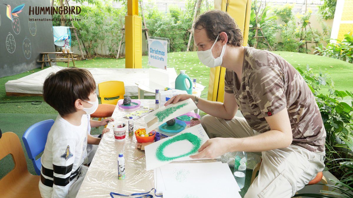 A man wearing a mask is sitting at a table with a child.