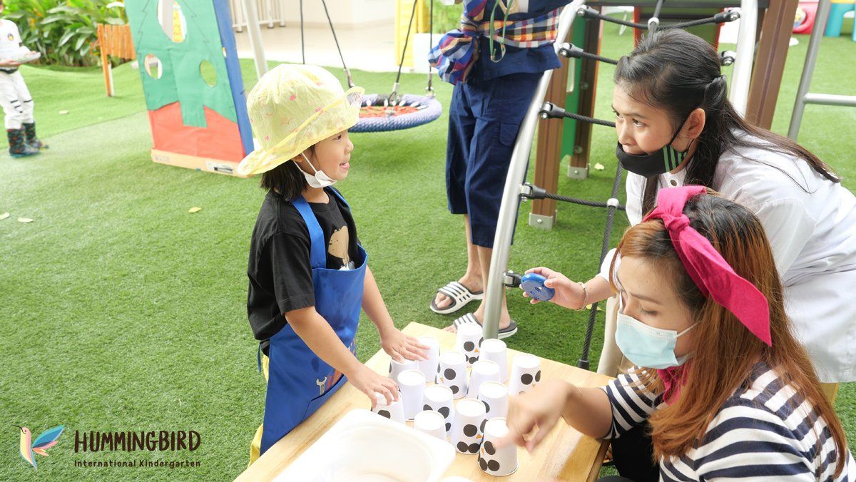 A group of people are standing around a table with a child wearing a mask.