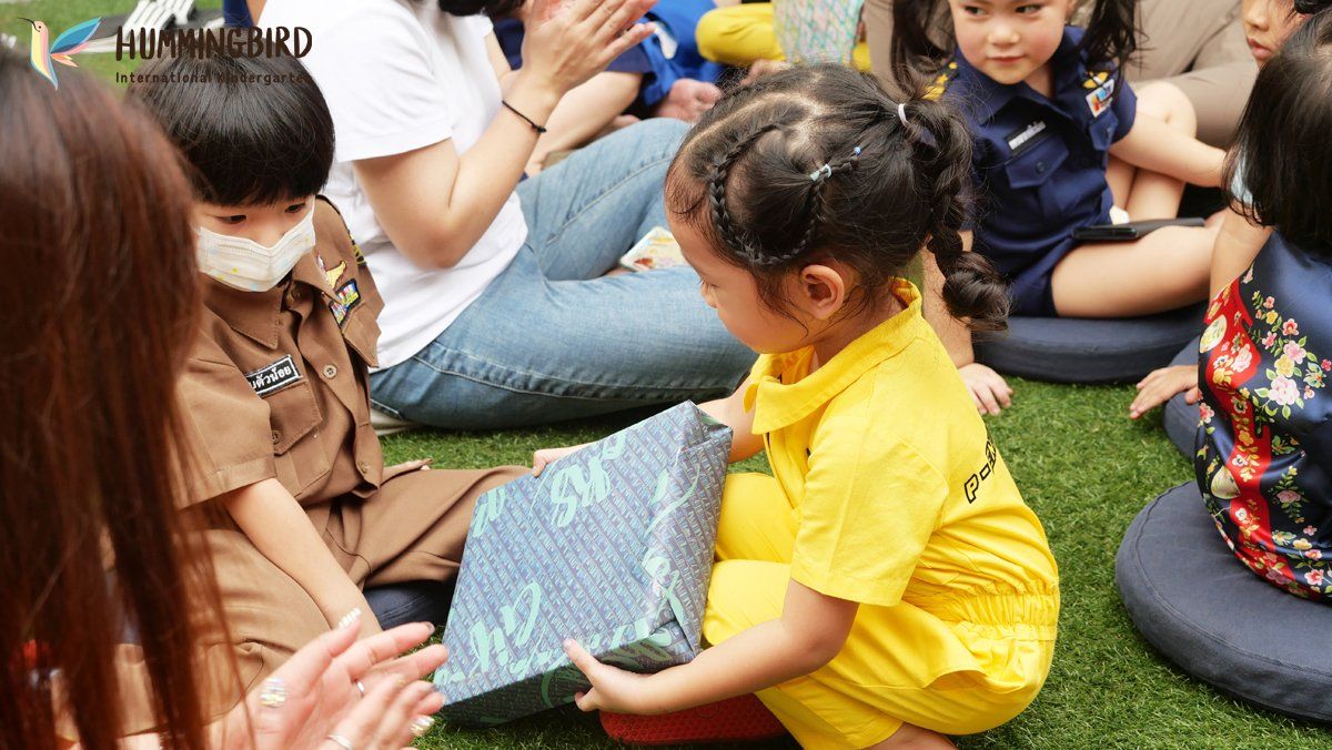 A little girl is sitting on the grass holding a gift box.