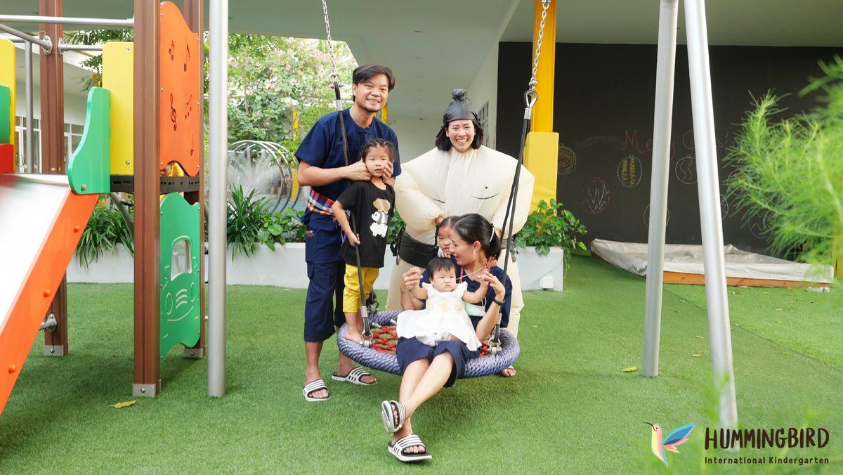 A family is sitting on a swing in a playground.