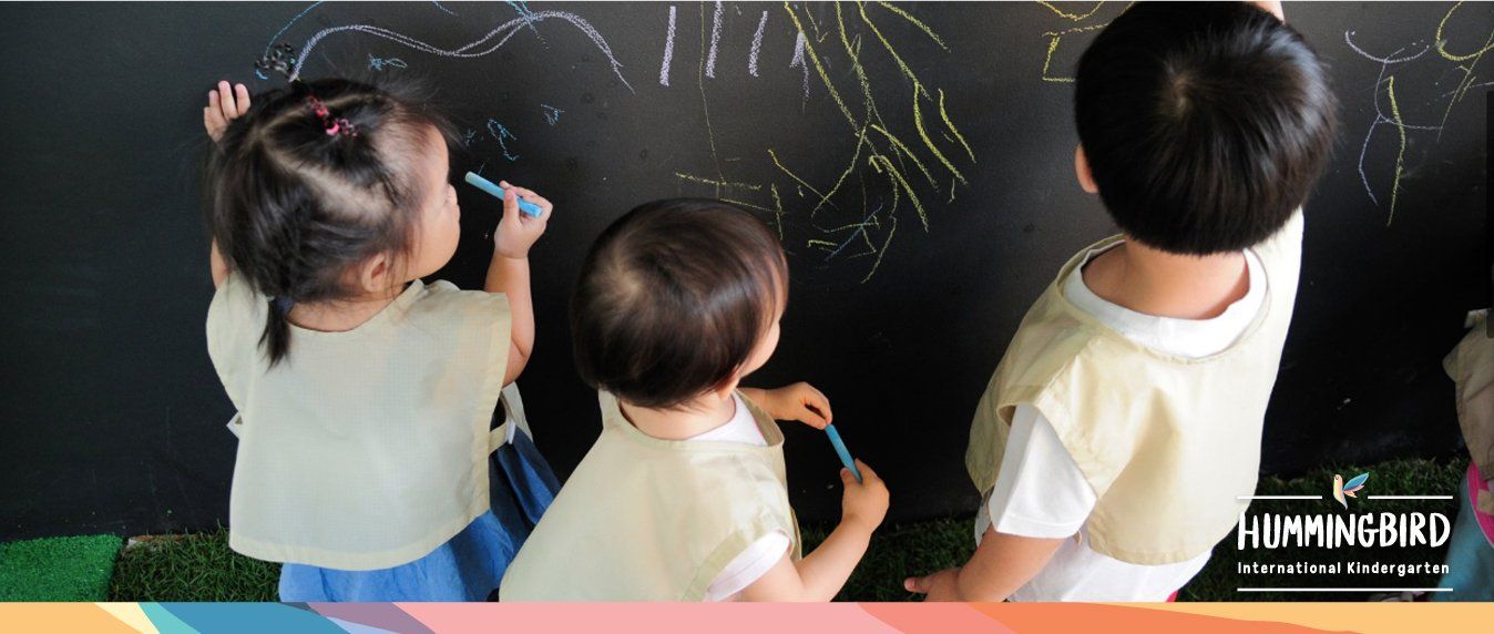 Three children are drawing on a blackboard with chalk.