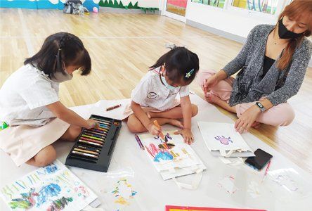 A woman and two children are sitting on the floor drawing.