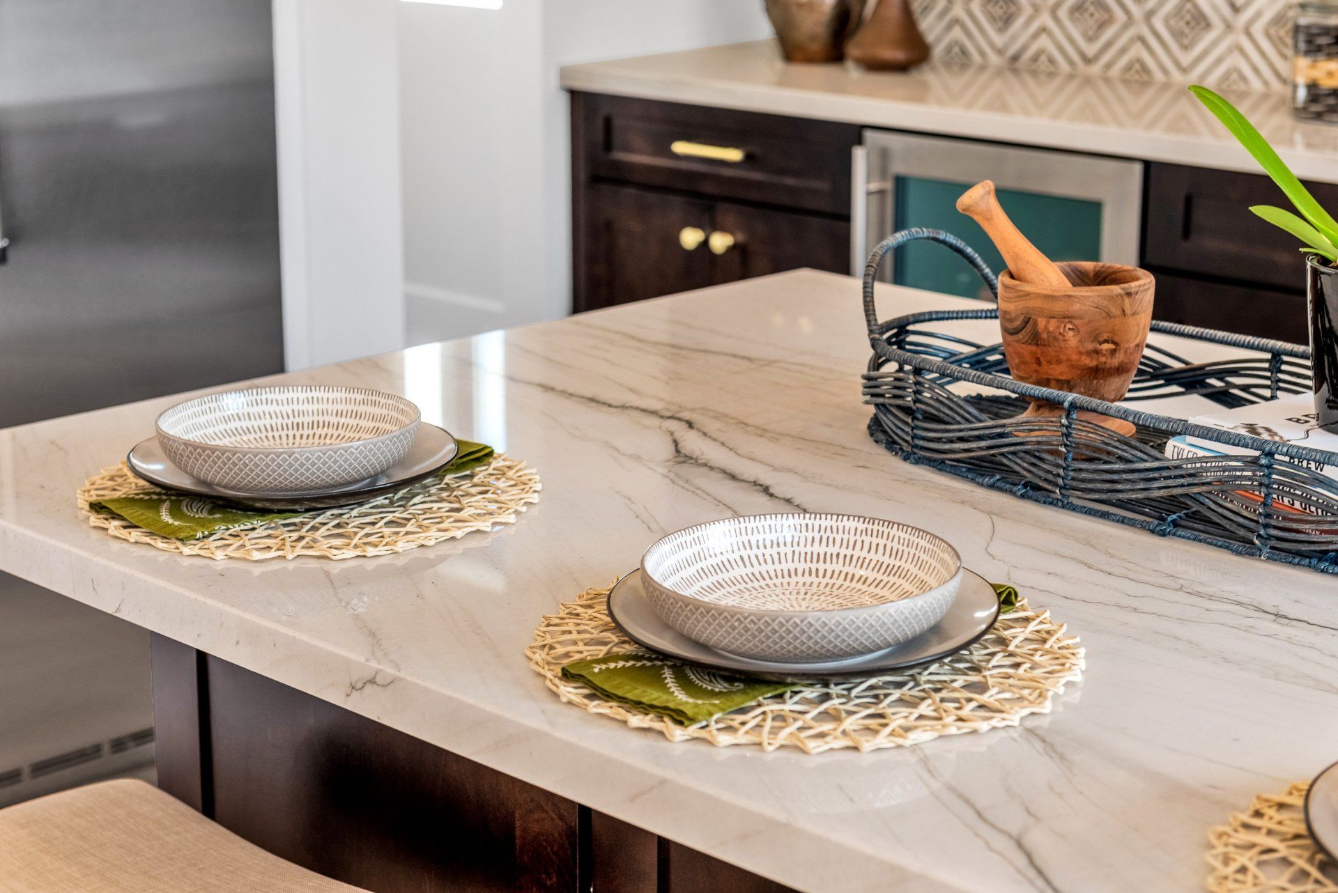 Kitchen island with place settings, woven placemats, and patterned bowls on a marble countertop.