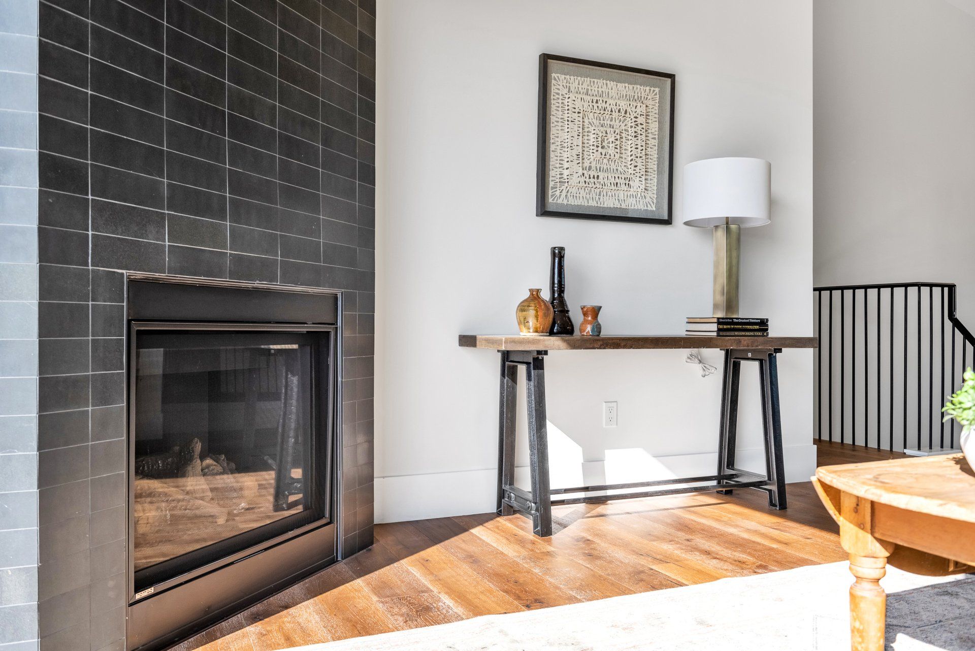 A living room with a black tiled fireplace and a table.