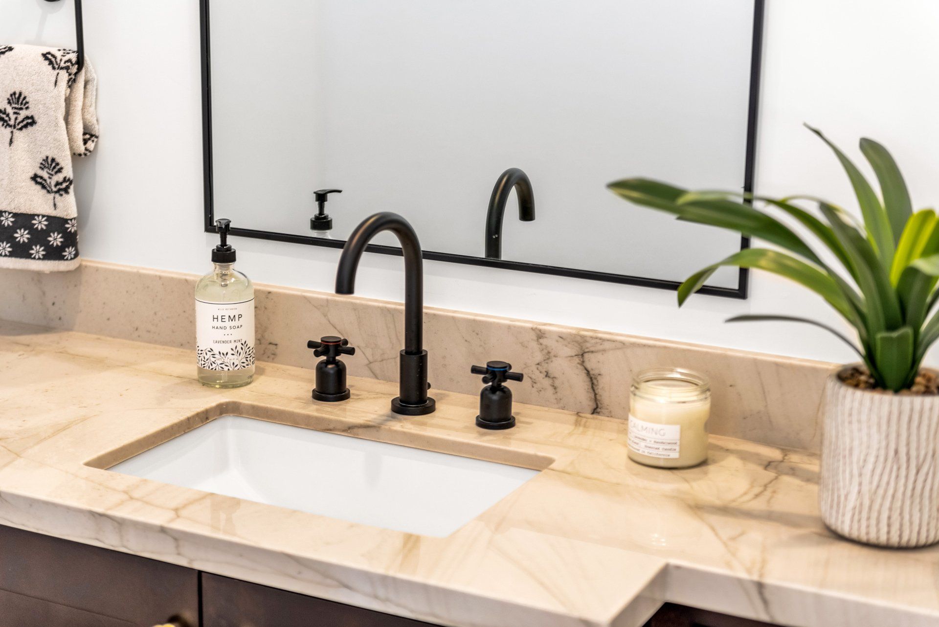 A bathroom sink with a plant and candle on the counter and a mirror.