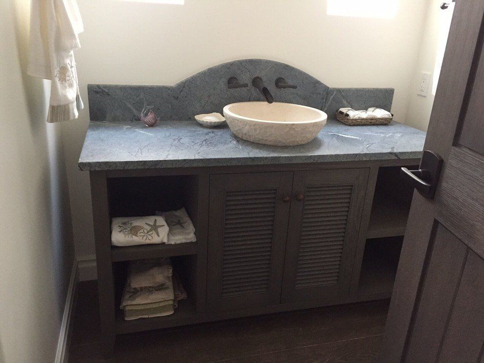 A bathroom with a natural stone sink and towels on the shelves.