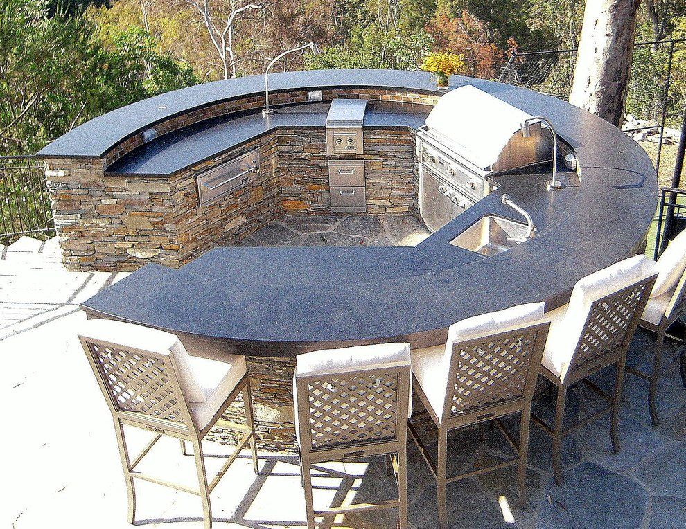 An outdoor kitchen with stone and black granite countertops with stainless steel appliances.