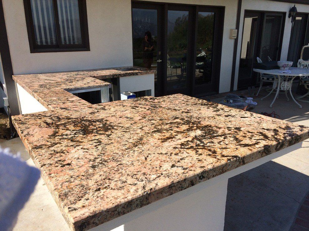 A large granite counter top is sitting outside of a house as an outdoor kitchen area.