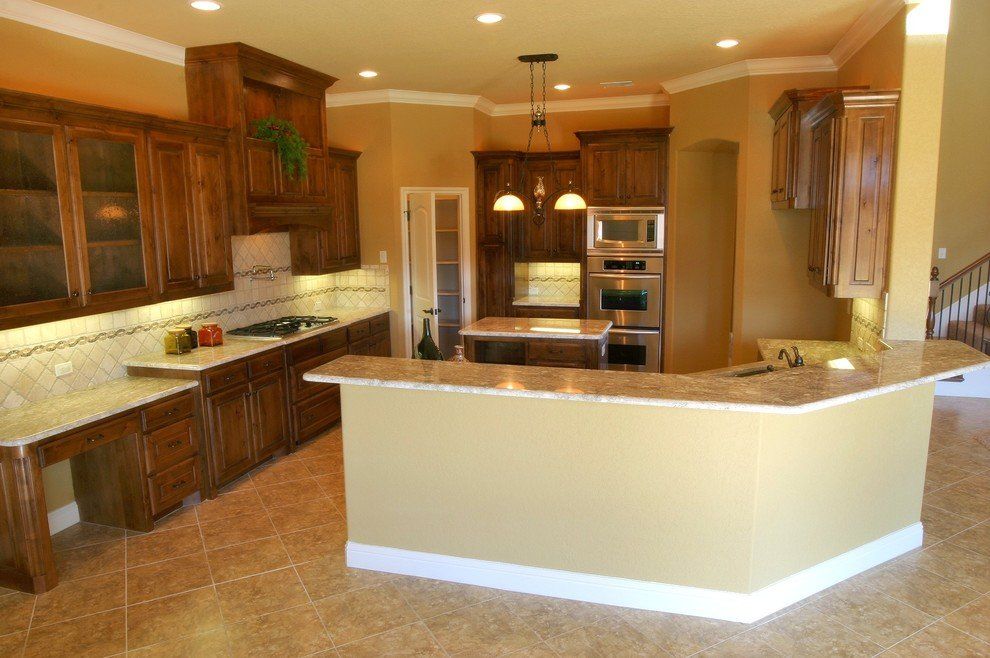 A kitchen with stainless steel appliances, wooden cabinets, and a wrap around counter with marble countertops.