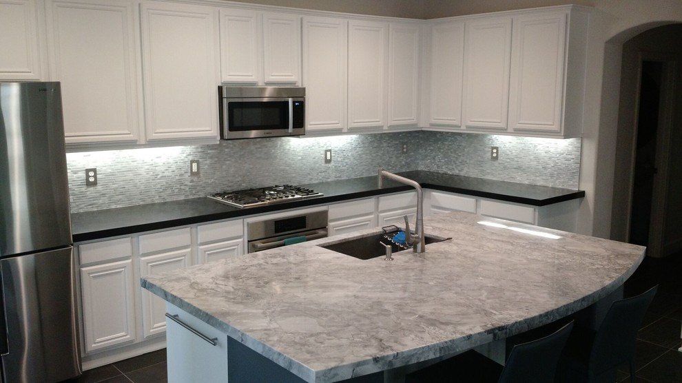 A kitchen with white cabinets , granite countertops, stainless steel appliances and a large island with a granite countertop.