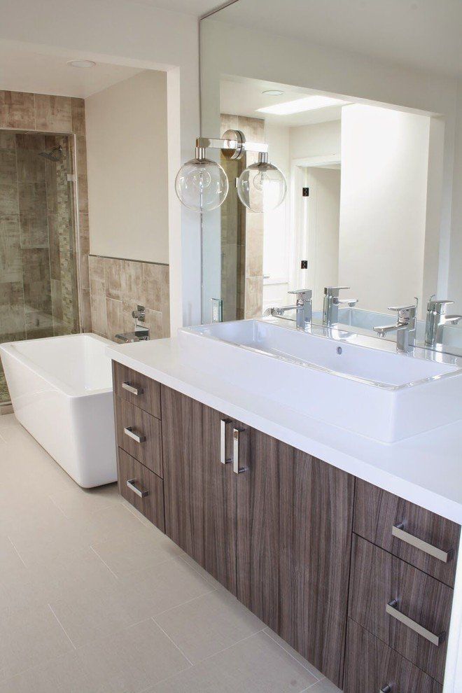 A bathroom with two sinks on a white countertop, a bathtub and a large mirror.