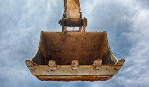 A rusty bucket is hanging from a crane against a cloudy sky.