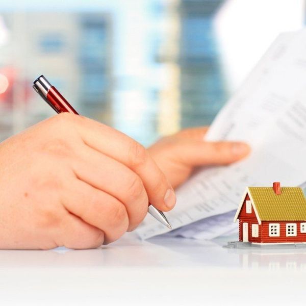 Human hand writing on a contract with a small house next to it.