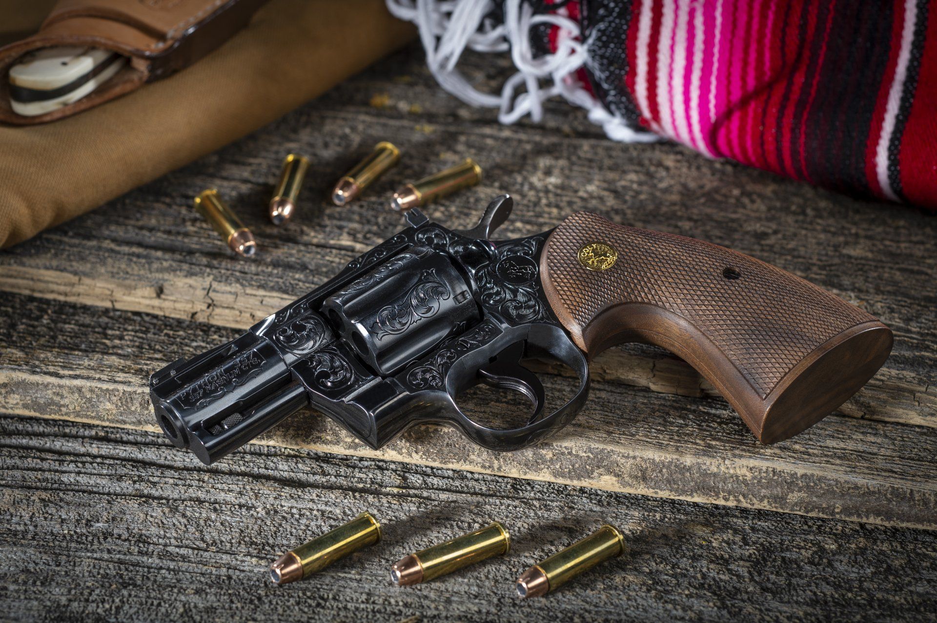 Black revolver with wood handle and bullets on a wooden surface with a red and white blanket.
