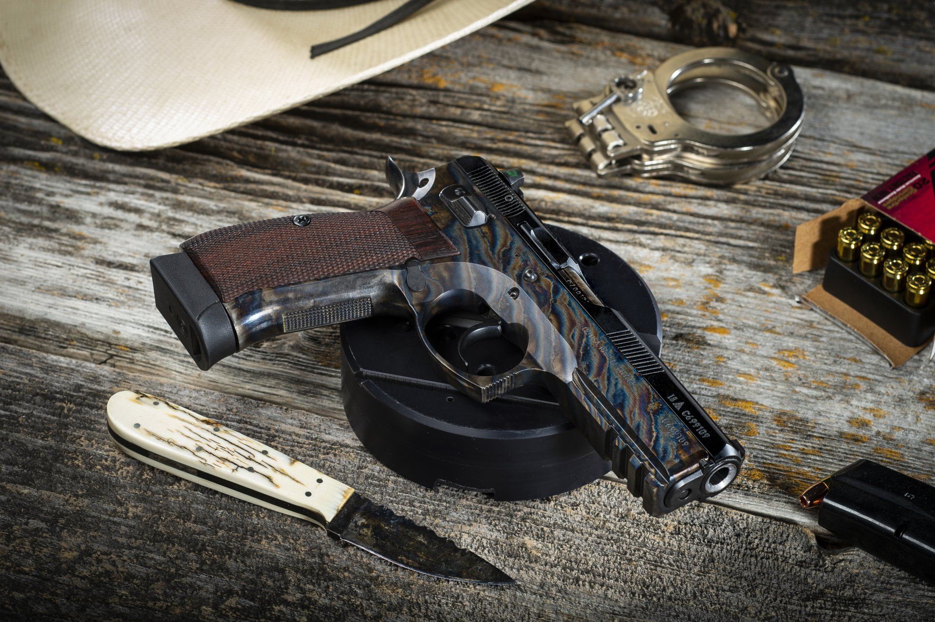 Gun, knife, handcuffs, bullets, and cowboy hat on weathered wood surface.