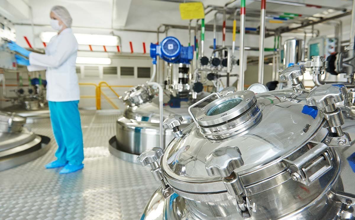 Científico con equipo de protección trabajando en una instalación de fabricación farmacéutica de acero inoxidable.