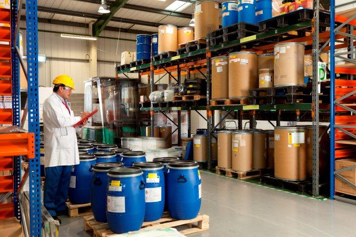 Trabajador del almacén inspeccionando barriles y contenedores en los estantes.