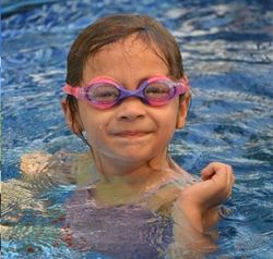 child wearing pink and purple swimming goggles while in the water. child wearing pink and purple swimming goggles while in the water.
