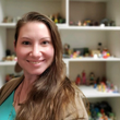 A woman is smiling in front of a shelf full of toys.
