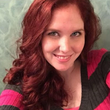 A woman with red hair is smiling and wearing a pink and gray striped sweater.