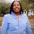 A woman with dreadlocks is wearing a blue shirt and smiling