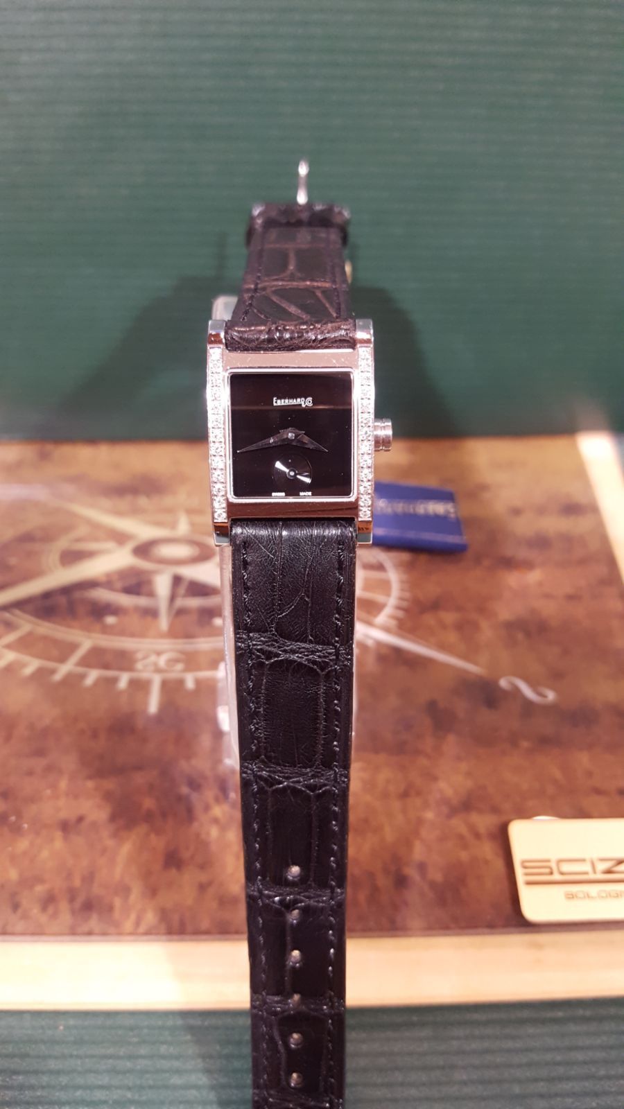 Orologio da polso rettangolare nero su superficie decorata; dettagli del cinturino e del quadrante visibili.