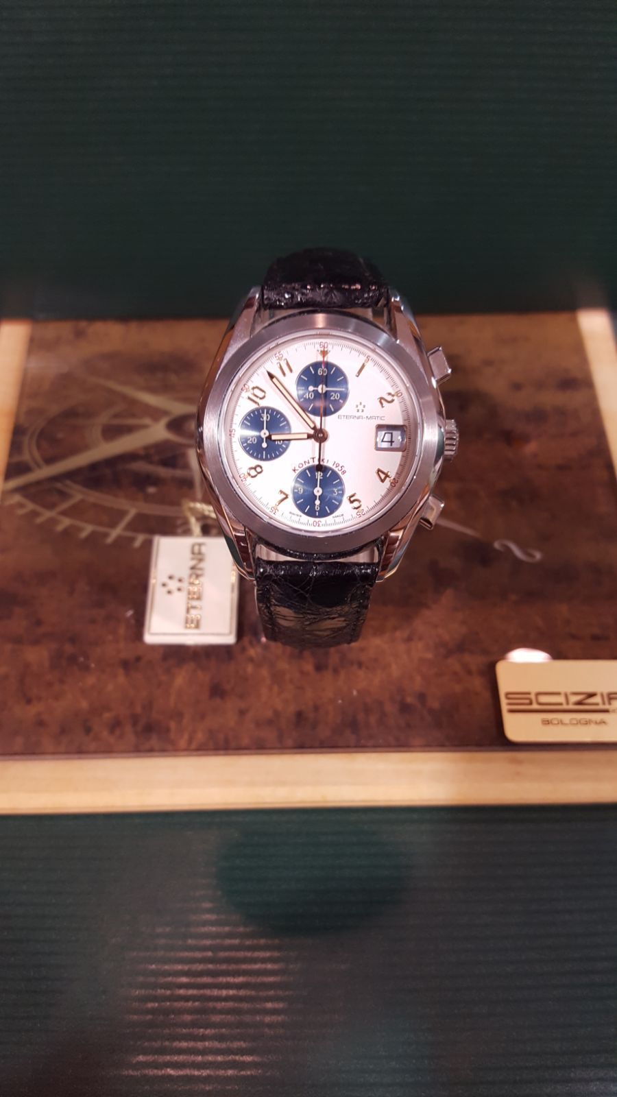 Orologio da polso cronografo in argento con quadranti secondari blu su una superficie in legno con etichetta.