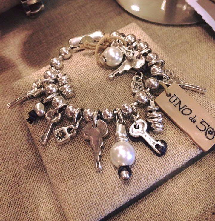 Braccialetto in argento con ciondoli a forma di chiave e perla, appoggiato su una superficie in tessuto testurizzato, con etichetta con marchio.