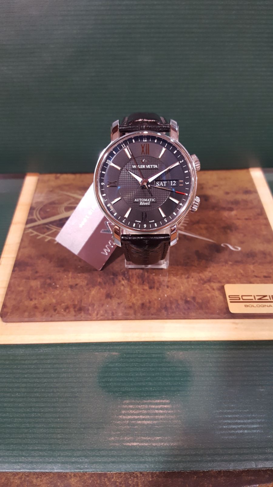 Un orologio da polso su un espositore di legno. L'orologio ha il quadrante e il cinturino neri, con l'etichetta del prezzo attaccata.