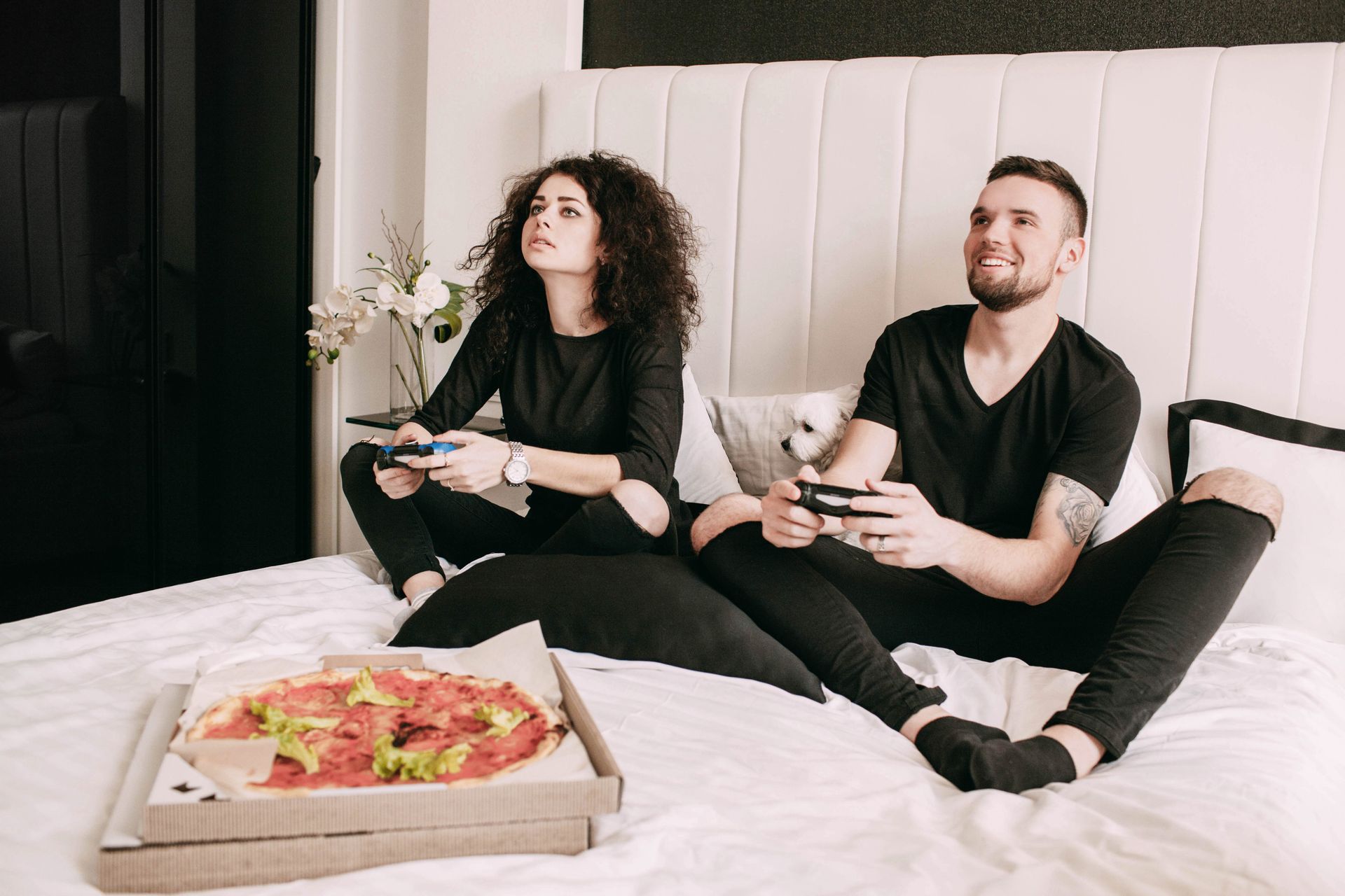 Stock photo of Young couple playing video games on a bed with a pizza nearby