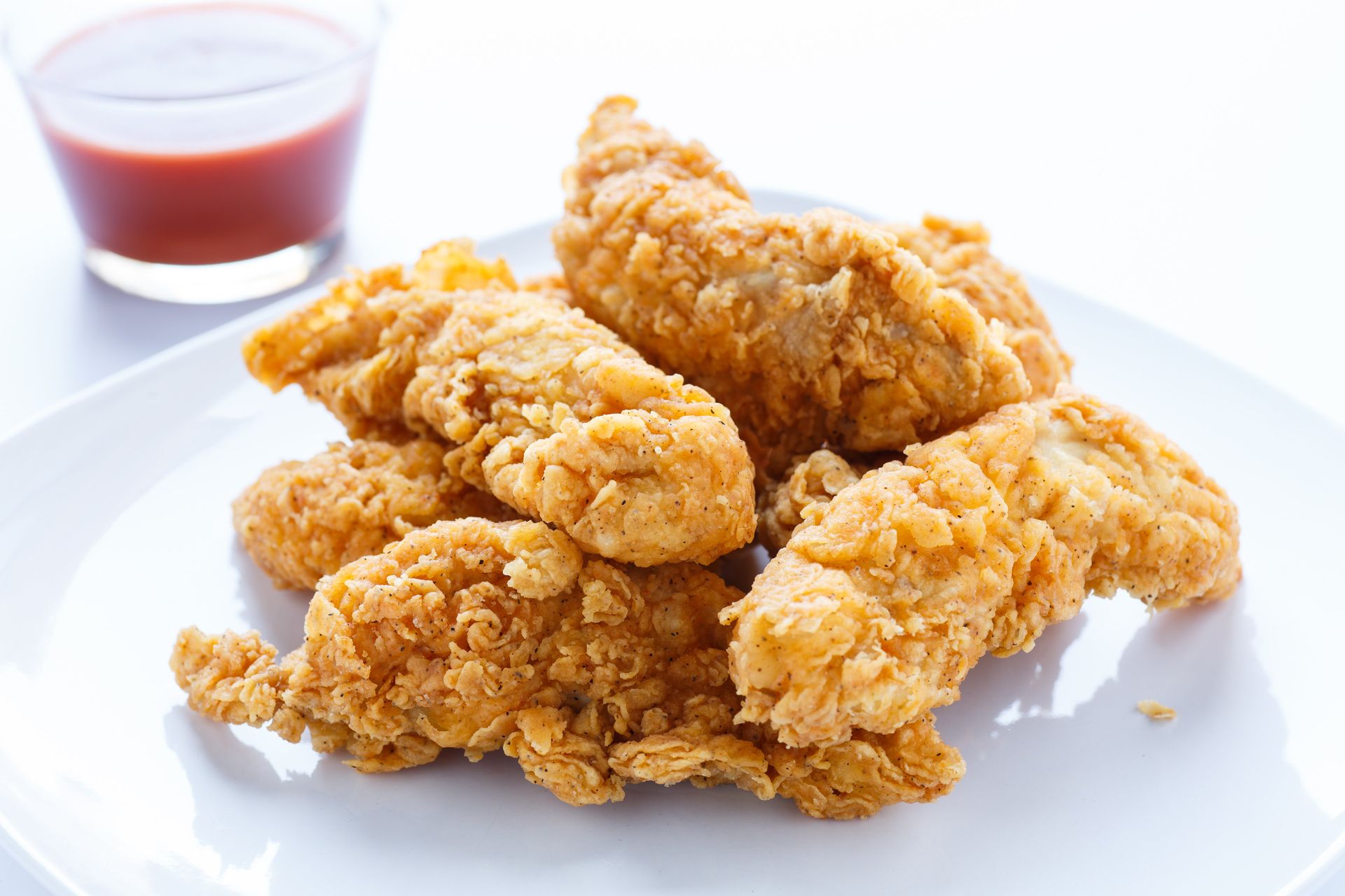 PHoto of chicken strips on a white plate with sauce in the background