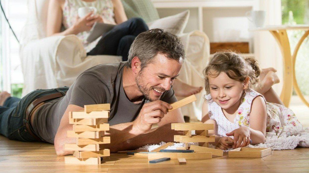 Father and child smiling while building a wooden block tower on the floor