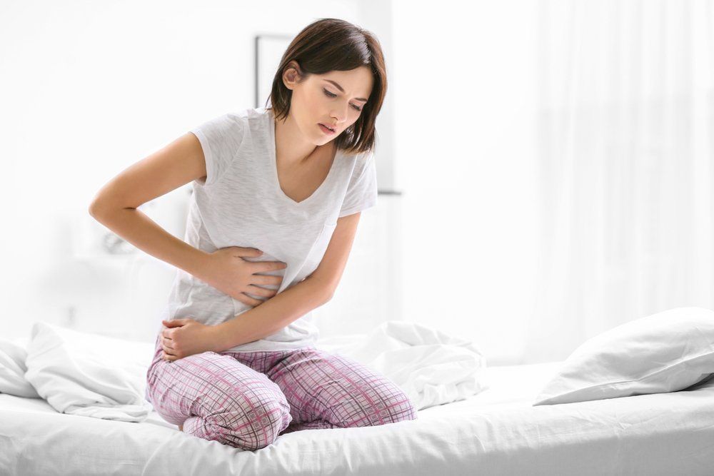 Eine Frau sitzt auf einem Bett und hält sich vor Schmerzen den Bauch.