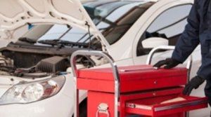 meccanico con carrello attrezzi si avvicina a un auto con il cofano aperto