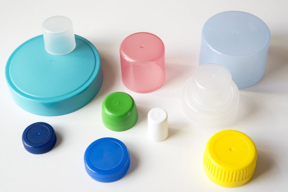 Tappi e coperchi di bottiglie di plastica colorati disposti su uno sfondo bianco.