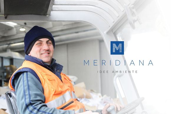 Un operaio con giubbotto di sicurezza arancione e berretto blu scuro si trova all'interno di un veicolo industriale bianco e sorride alla telecamera.