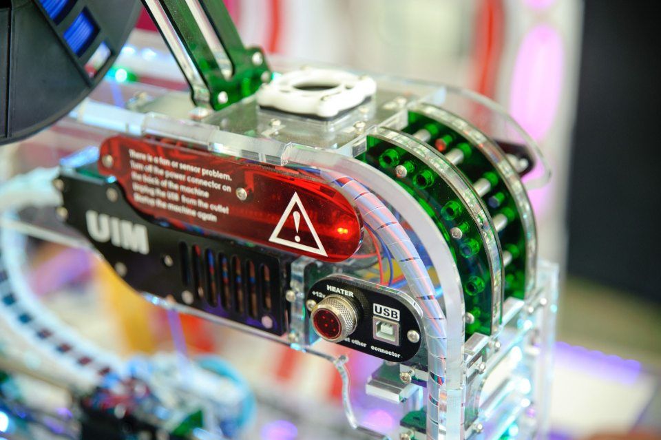 Primo piano di un circuito stampato rosso e nero con LED verdi luminosi e un'icona a forma di triangolo di avvertimento.