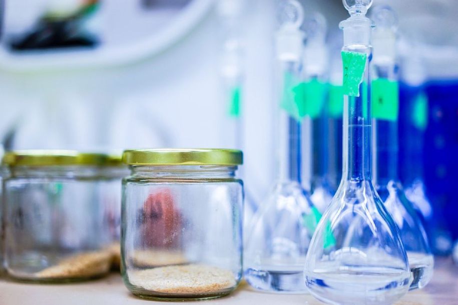Vetreria da laboratorio con liquido blu e due barattoli di campioni su un banco da laboratorio.
