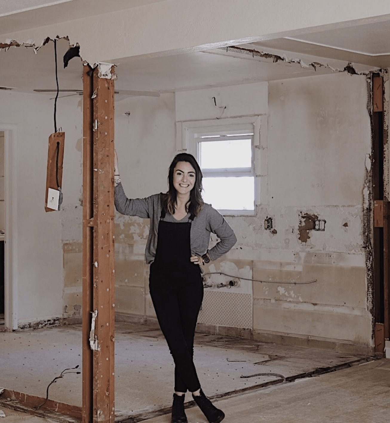 Debbie Mayes stands smiling in the gutted kitchen of their modern small kitchen remodel.