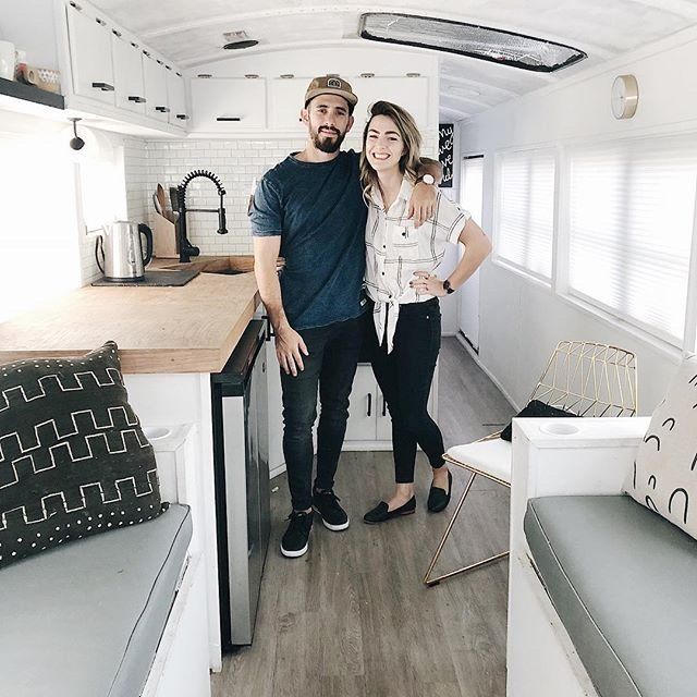 Debbie and Gabriel Mayes stand side by side in their skoolie bus kitchen smiling about school bus conversion cost.