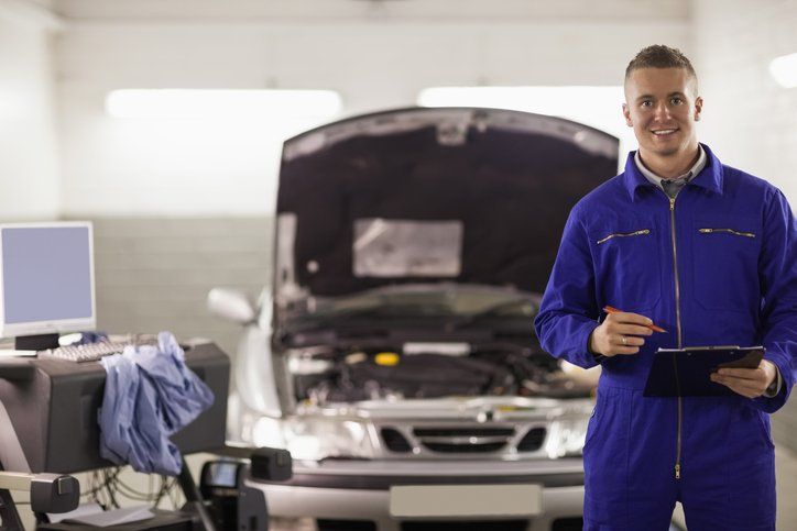 Smiling mechanic holding a clipboard next to a car - Auto Repair in Bay City, TX Smiling mechanic holding a clipboard next to a car - Auto Repair in Bay City, TX